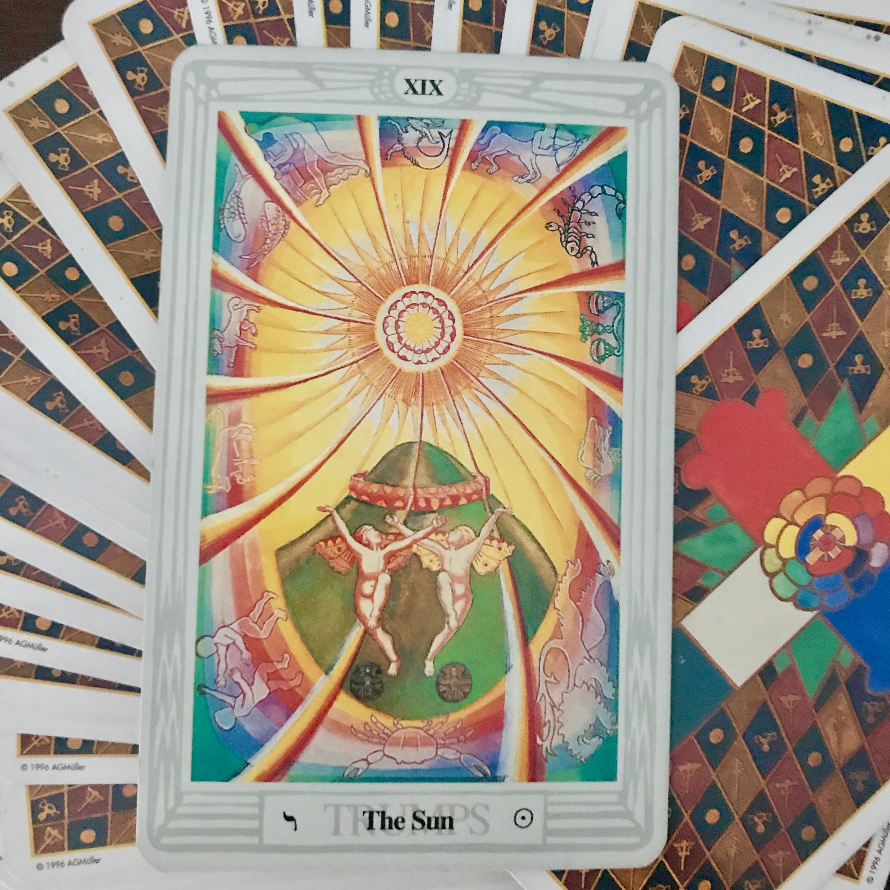 This card is from a Thoth Tarot Card deck and depicts the major arcana SUN.  The colors are bright yellow with optimistic red ribbons reaching out to the border with angels dancing, arms up, looking toward the central sun. 