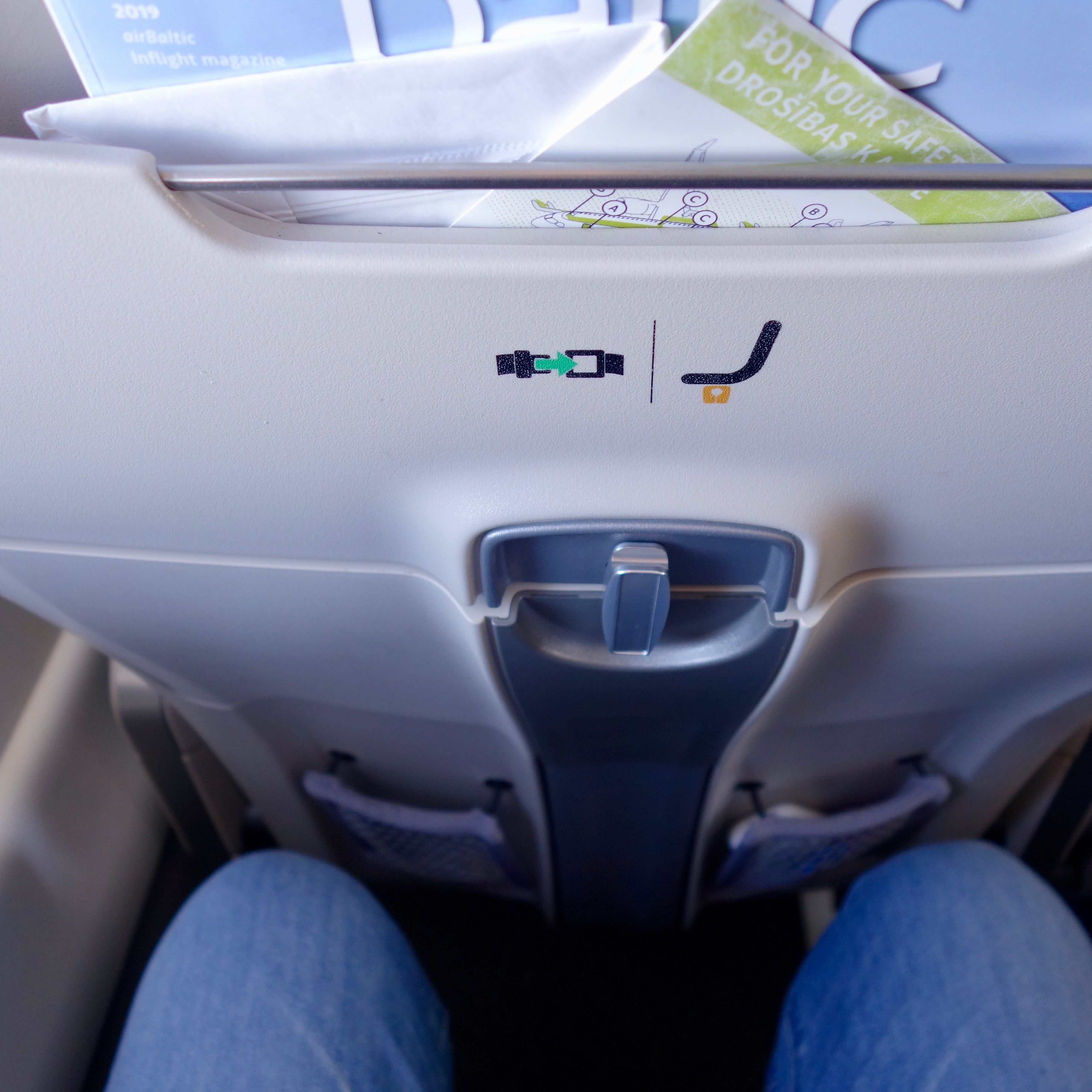 This photo is designed to review the amount of legroom available on the airBaltic Airbus A220 aircraft. In this case, the knees of the passenger do not touch the seat ahead, indicating legroom is comfortable enough for a short flight.  
