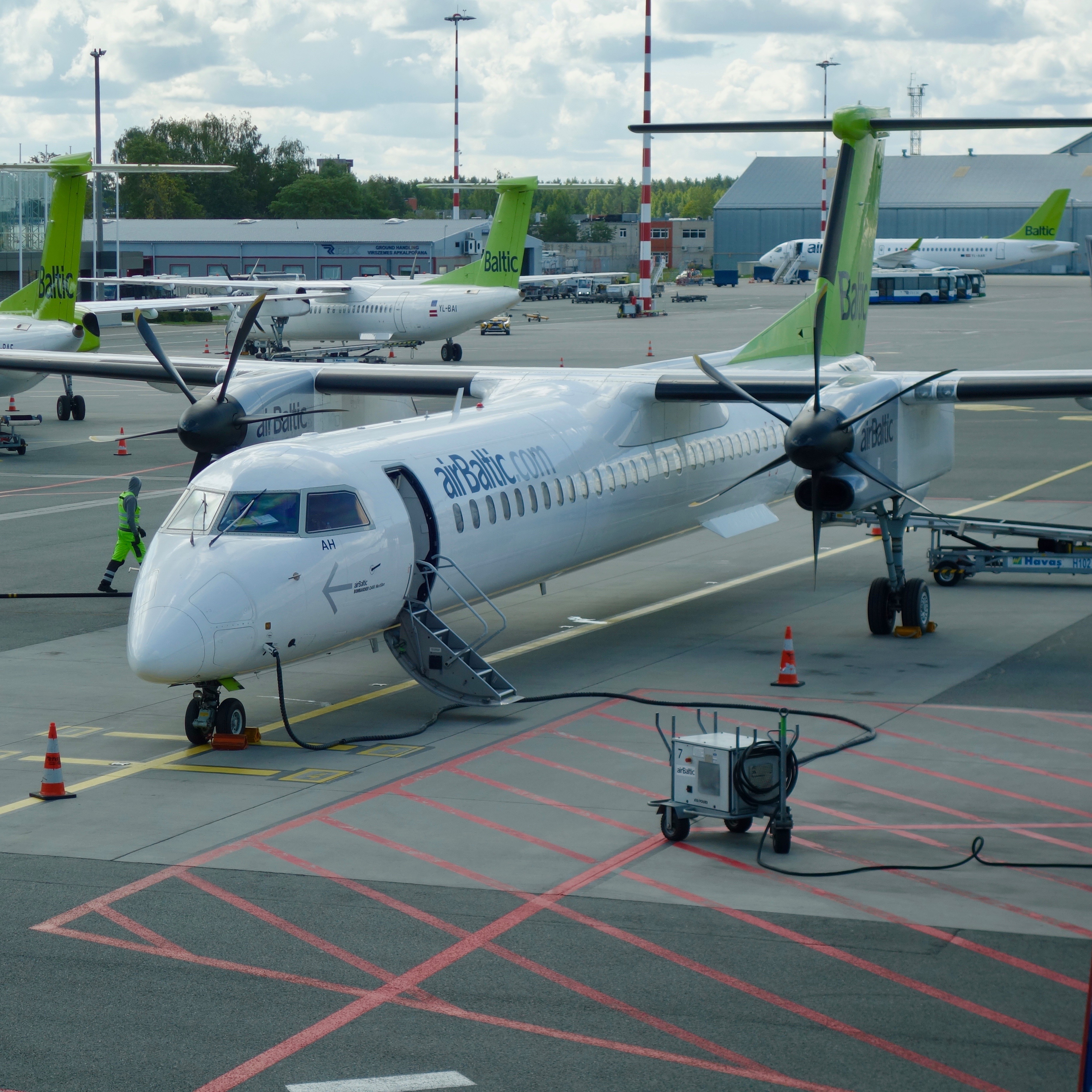 This shot features a Bombardier Q400.  The aircraft has two prominent black propeller turbines supporting the narrow fuselage tube while the green colored tail rises up in the background.  There are several other Q400s in the background. 