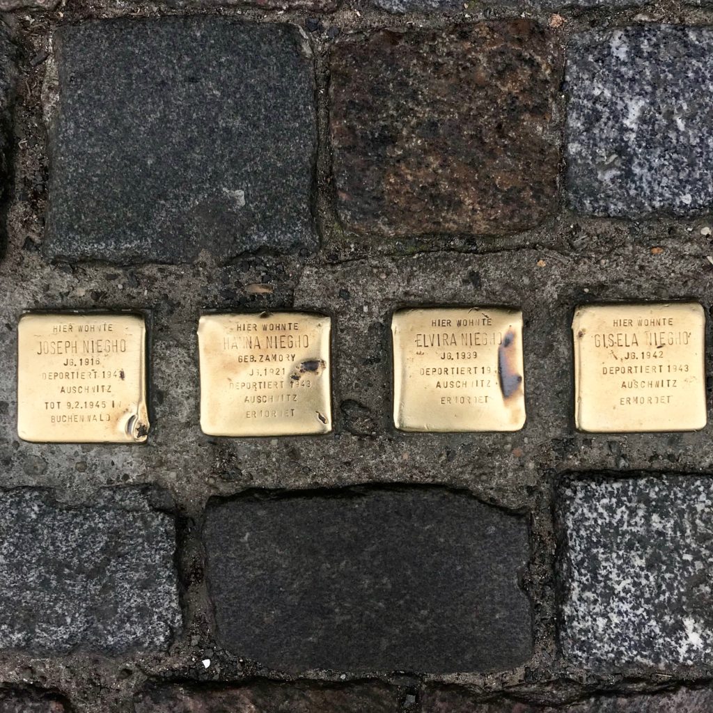 Four copper tiles on a cobblestone street in Berlin that memorialize Jewish citizens taken to Auschwitz during WWII