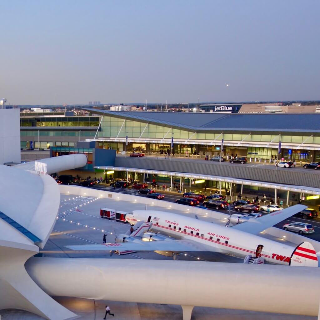 View looking down from the pool deck of the TWA Hotel over looking the iconic Eero Saarinen JFK Airport Terminal completed in 1962 for TWA. Outside the terminal is a vintage TWA Super Constellation, also know as the "Connie."