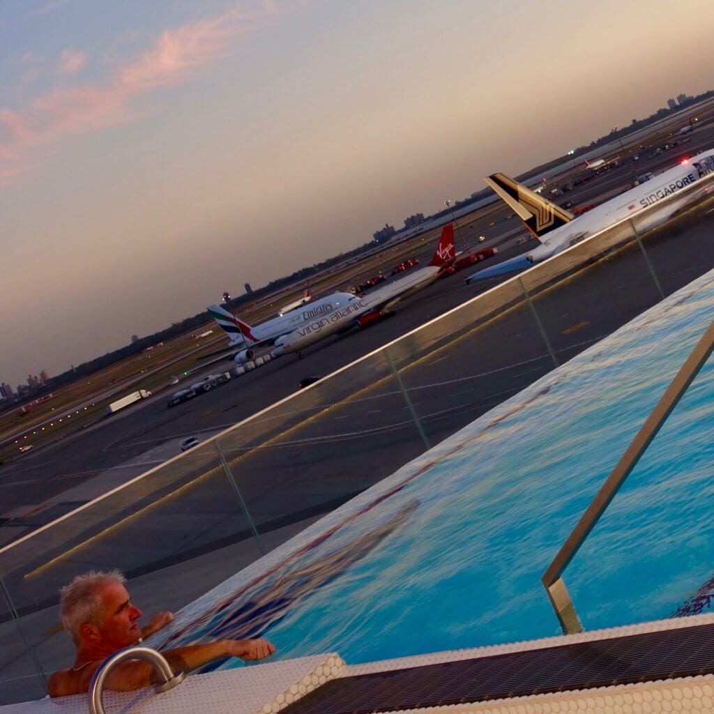 The pool deck level of the TWA Hotel, near JFK Terminal 5 overlooks the ramp area and airplanes. The pool is narrow rectangle shape and the water warm.