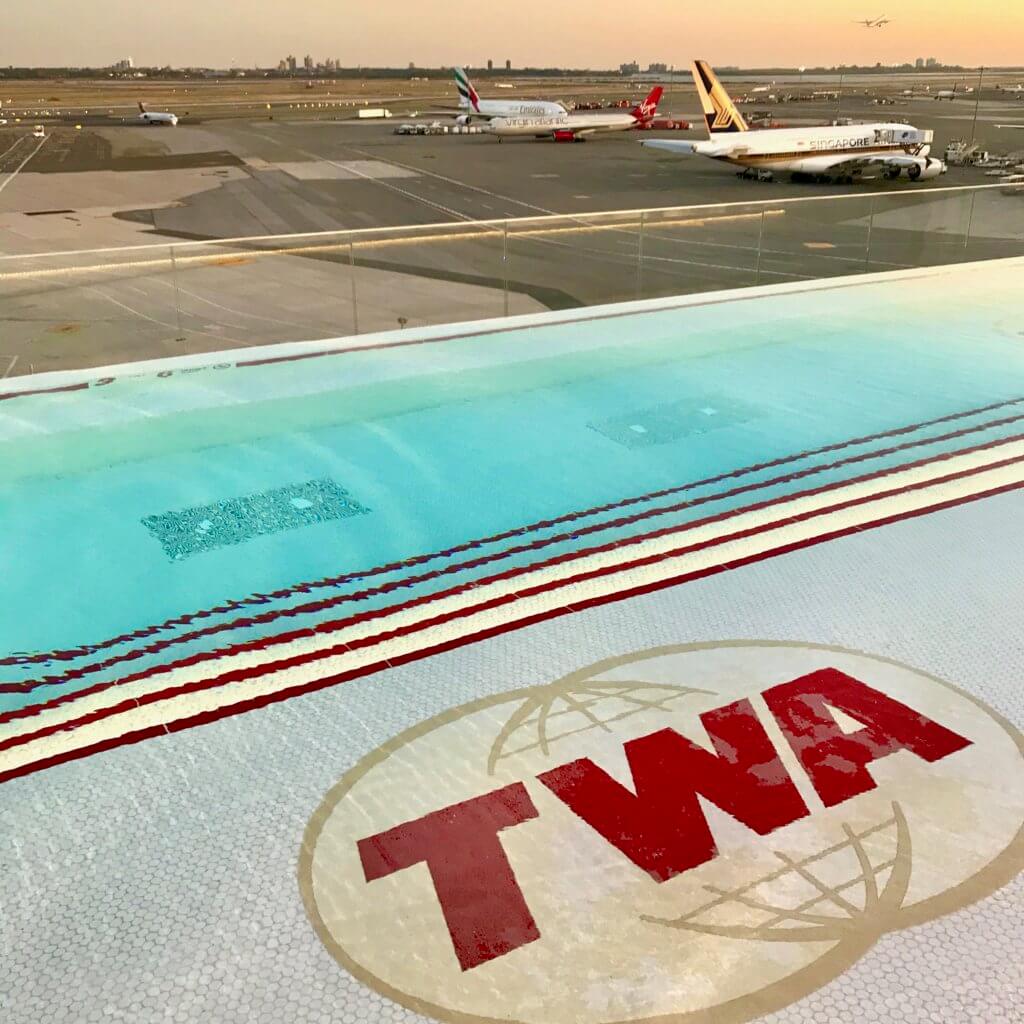 The pool deck level of the TWA Hotel, near JFK Terminal 5 overlooks the ramp area and airplanes. The pool is narrow rectangle shape and the water warm.