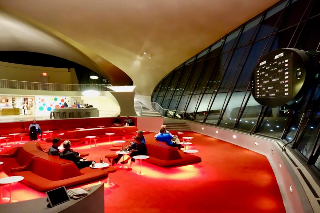 A sweeping nighttime view of the Sunken Lounge, which looks upon a high vaulted wall of windows out into the nighttime ramp area. This is a prominent feature of the Eero Saarinen Terminal built for TWA in 1962. It is now part of the TWA Hotel at JFK Airport.