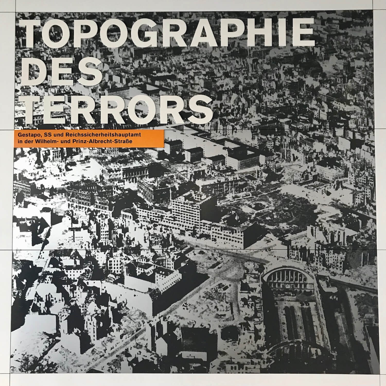 Entrance sign to the Topographies des Terrors exhibit in Berlin, Germany. This square poster shows a black and white photo of Berlin before World War two.
