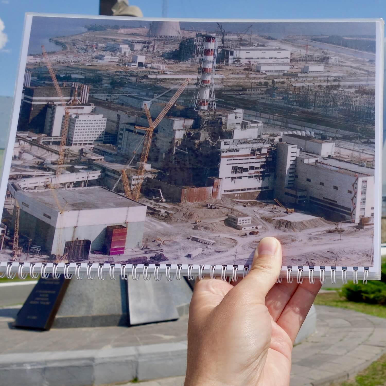 Photo on a spiral notebook of Chernobyl reactor #4 shorter after the steam explosion in April 1986. In the background is the current view of Chernobyl Reactor 4, which is now covered up with a titanium sarcophagus.