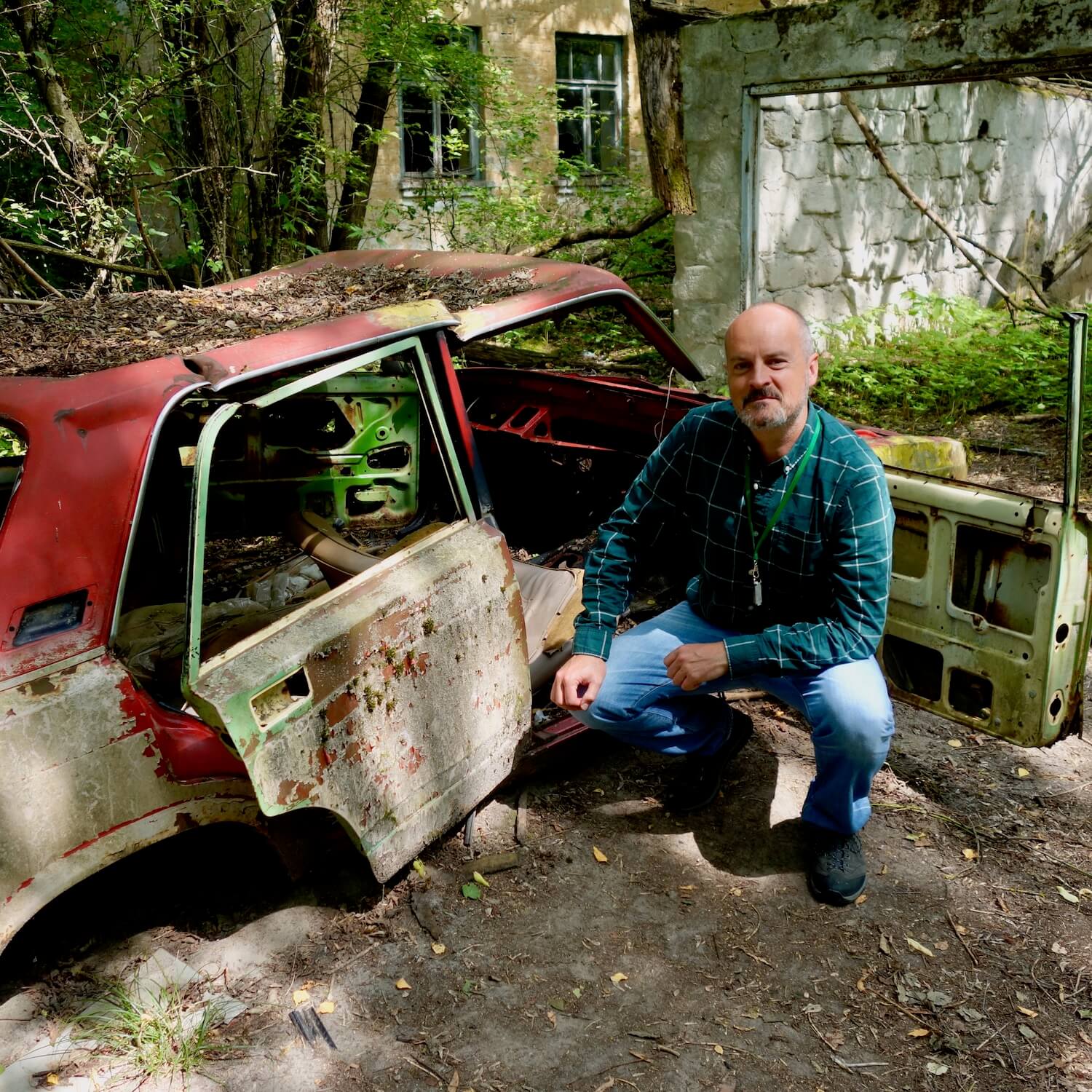 I am squatting next to an old Russian Lara car left behind after the Chernobyl explosion. This is located within the Chernobyl exclusion zone.