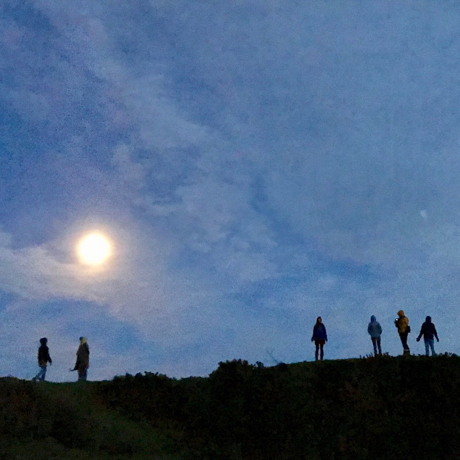 The moon rises over the sacred mound at Dowth on the eve of the longest night of the year. The glow creates a backdrop for six people standing atop the mound.