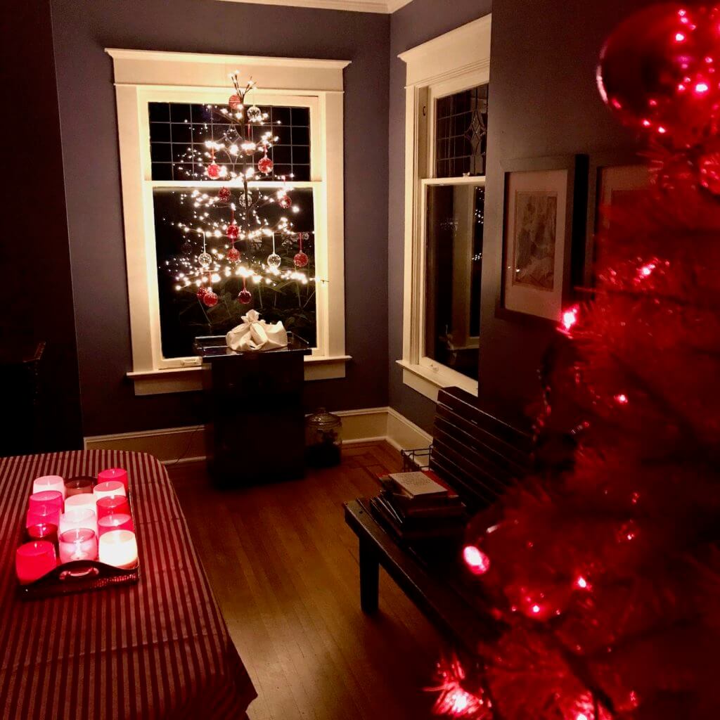 House all set up for the holiday with a tray of glassy baby on the dining room table and a lighted tree in the window of the house.
