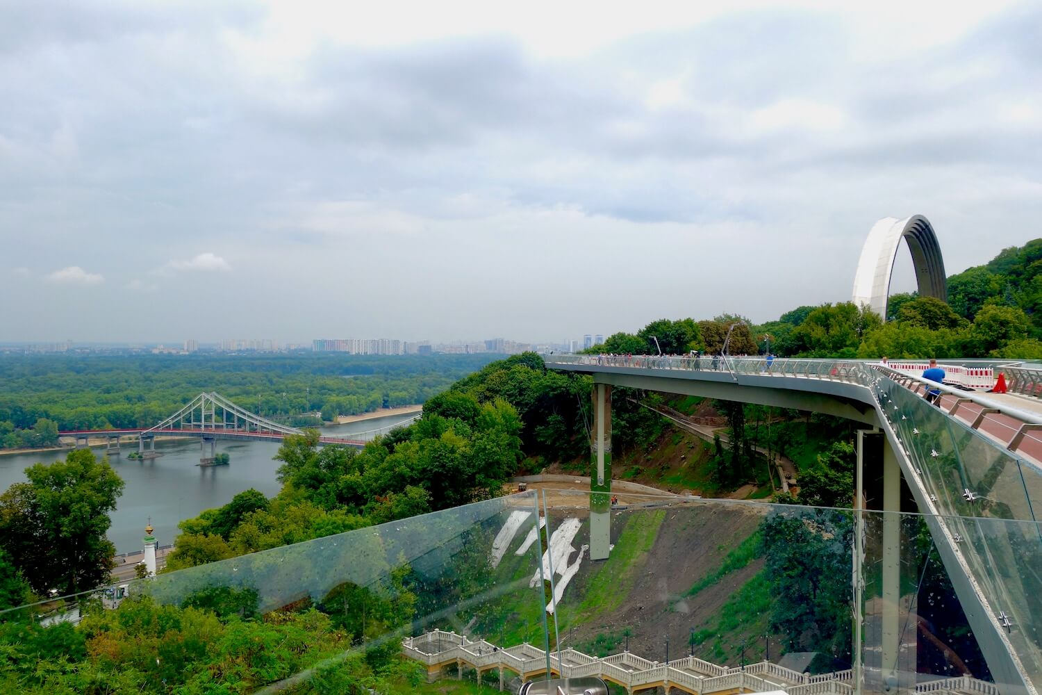 The view from Volodymyr Hill, which includes the new Glass Bridge crossing the ravine to the Friendship Arch.  The view downhill focuses on the Dnieper River. 