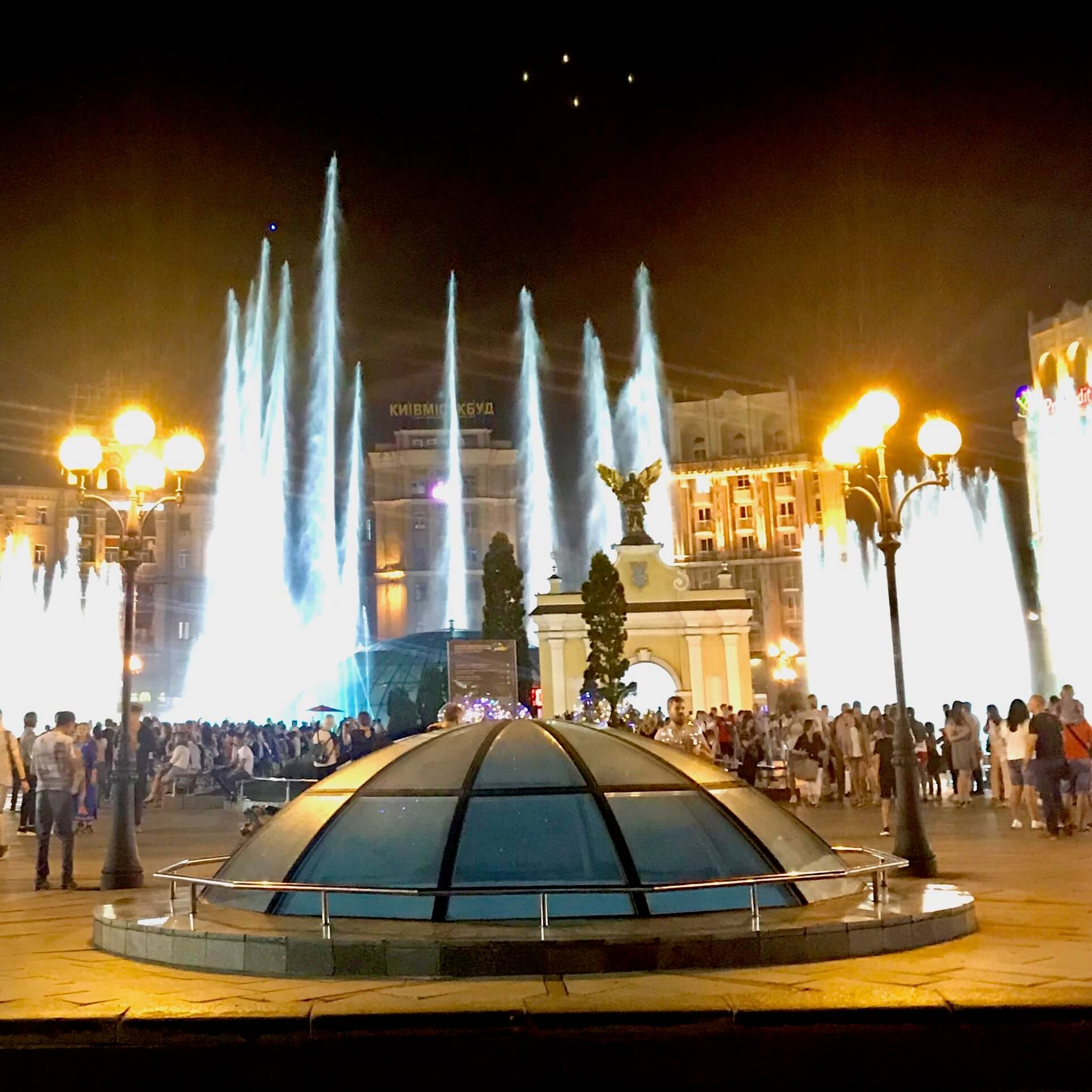 Large cannons of water spray up in a busy nighttime Independence Square in central Kiev.