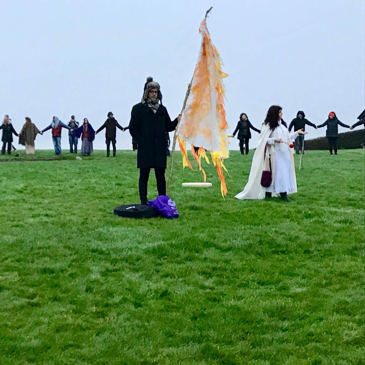 At winter solstice in Newgrange Ireland sunrise participants gather in one large circle around a woman in a white dress who strikes a gong to welcome in the new year.