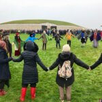 Groups of solstice goers hold hands in circles directly outside the entrance to ancient Newgrange.