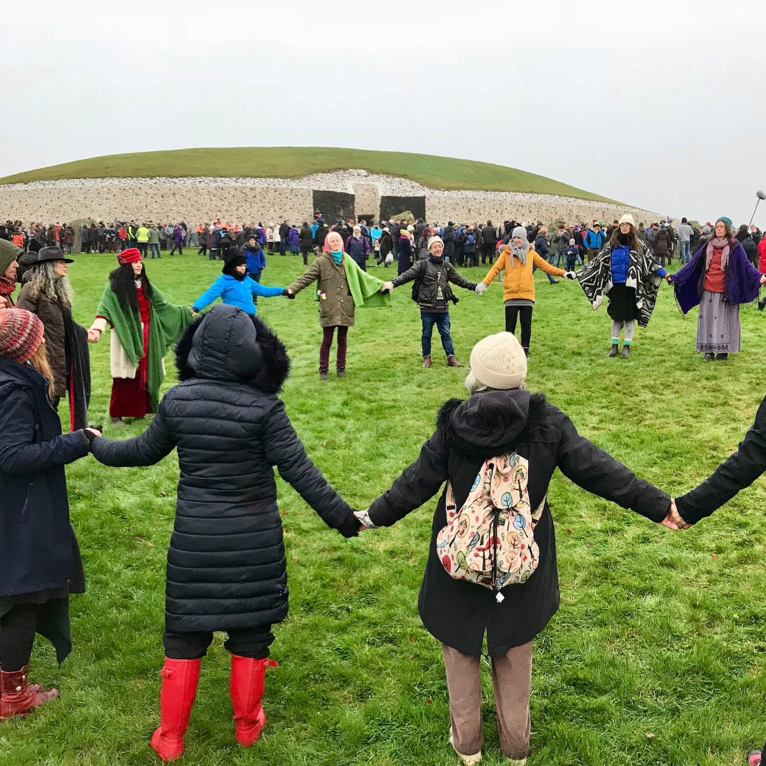 Groups of solstice goers hold hands in circles directly outside the entrance to ancient Newgrange Ireland during the winter solstice.