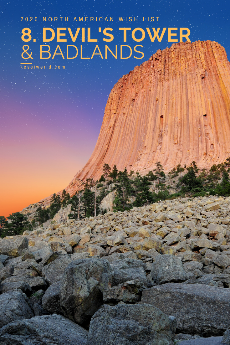 Devil's Tower landmark is the prominent feature of this photo, with a multi-colored sunset of oranges and purples in the background and sharp granite broken rocks in the foreground.