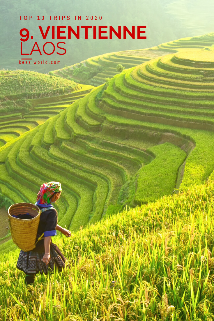 Number on the global list of destinations for 2020 is Vientienne, Laos. A woman walks up a lush green hill of rice with a basket on her back.