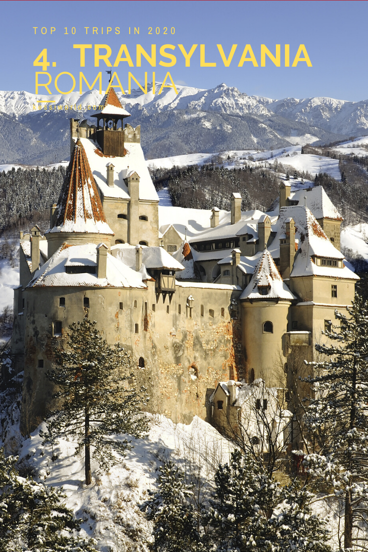 This wintry scene features bran castle in Transylvania covered with a dusting of snow with snow covered mountains rising up in the background.
