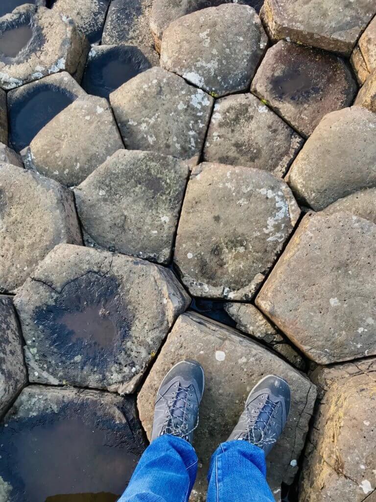 The Giant's Causeway is an area of about 40,000 interlocking basalt columns which are shown in this photo. My legs and shoes are shown standing on one of the rocks amongst all the other pentagon shaped stones.