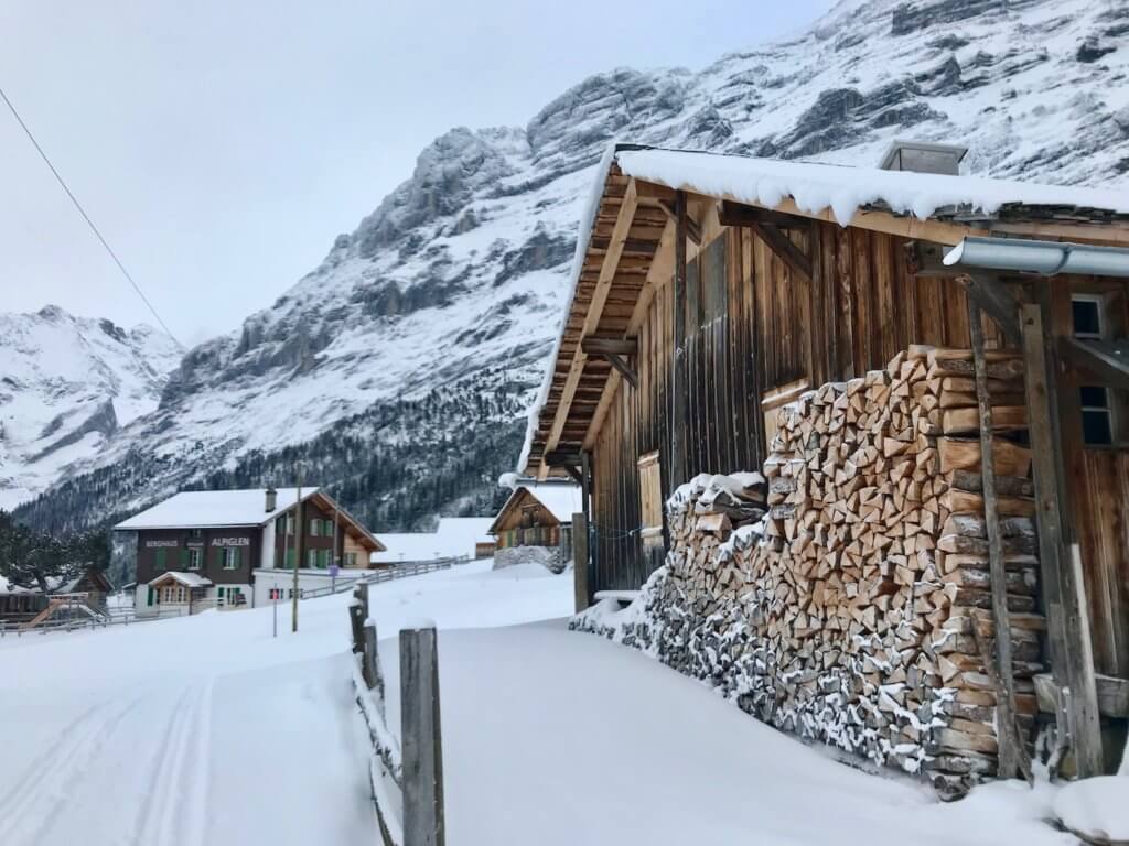Walking up upon a Swiss barn with stacked wood pile and a mountainside restaurant inn in the far distance. All under the rocky peak of Eiger.