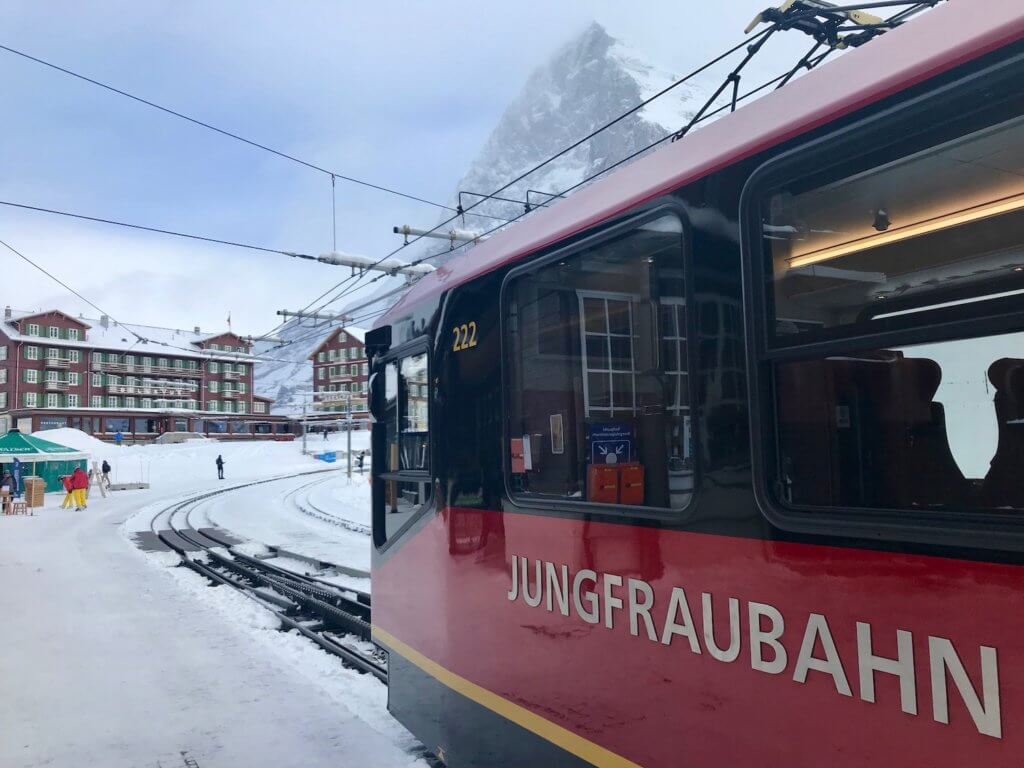 Gleaming red Jungfraubahn, narrow gauge rail heading toward the Top of Europe tourist attraction. In the background are the hotels and other resort buildings in the alpine hamlet of Kleine Schiedegg.