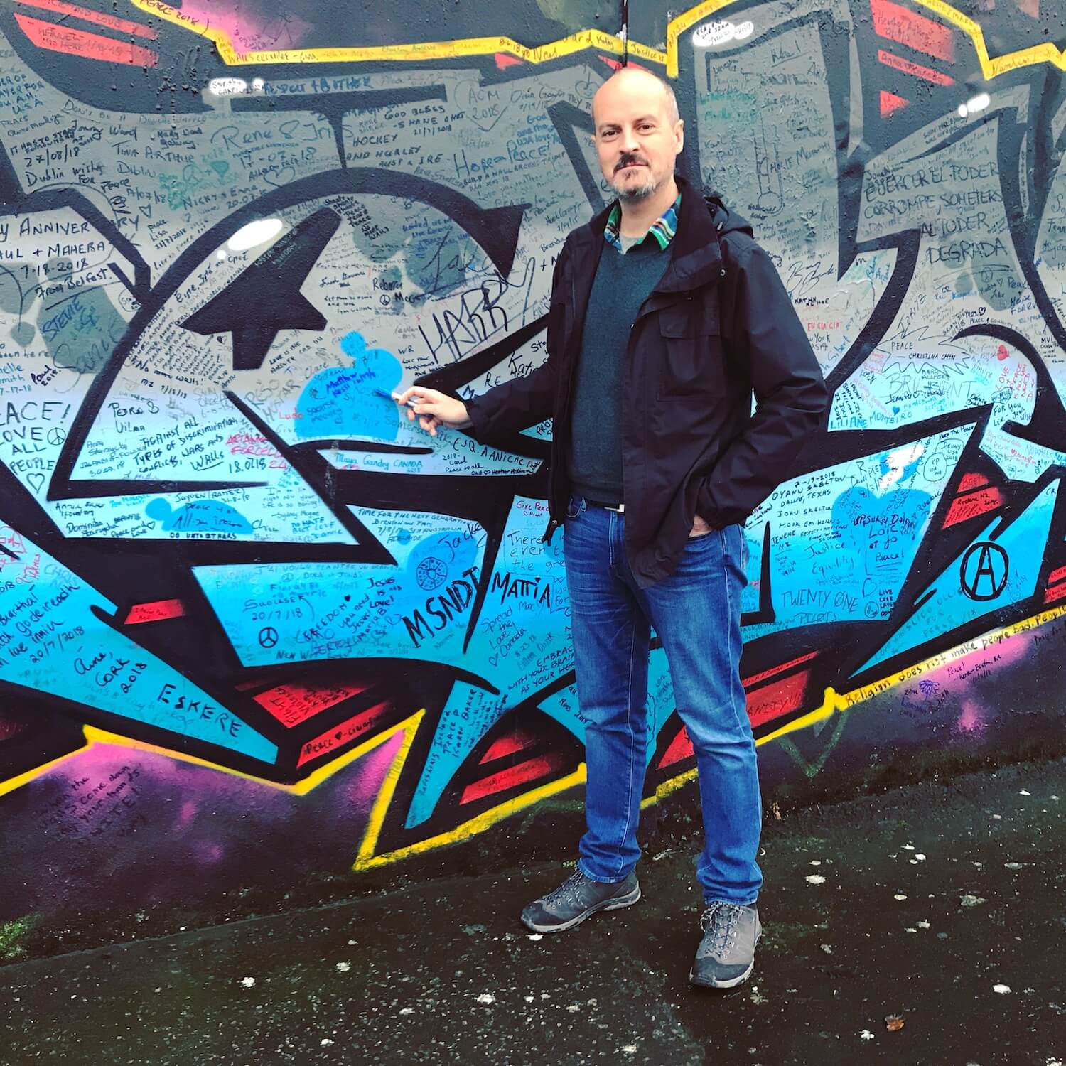 I stand at a remaining piece of the physical wall that used to divide Belfast into a Catholic area and a Protestant area. There is a variety of graffiti on the wall and I'm holding a pen that points to my fresh signature and date on the wall.
