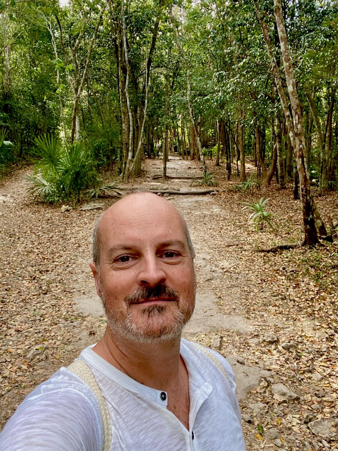 Matthew Kessi walking along the ancient white limestone Sacbé 9 which was used by the Mayans to travel between places.  Jungle life continues to push through the roadway with dense foliage of trees. 