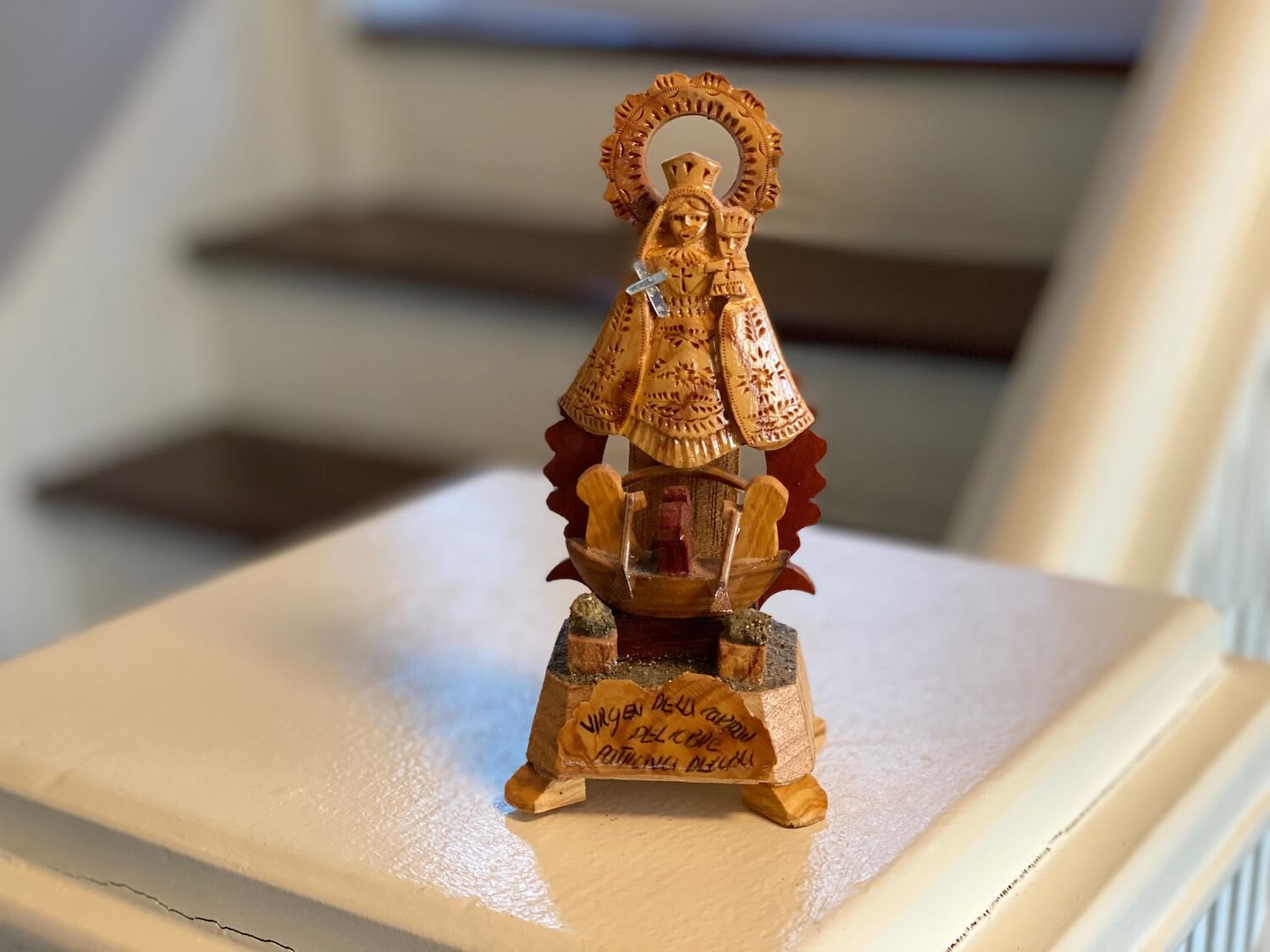 This travel souvenir from Cuba was picked up near Santiago at the National Shrine Basilica of Our Lady of Charity. It has soul and is carved from local wood and depicts Mary, with a silver cross appearing above a boat with two fisherman rowing. Mary has a circular halo above her head.