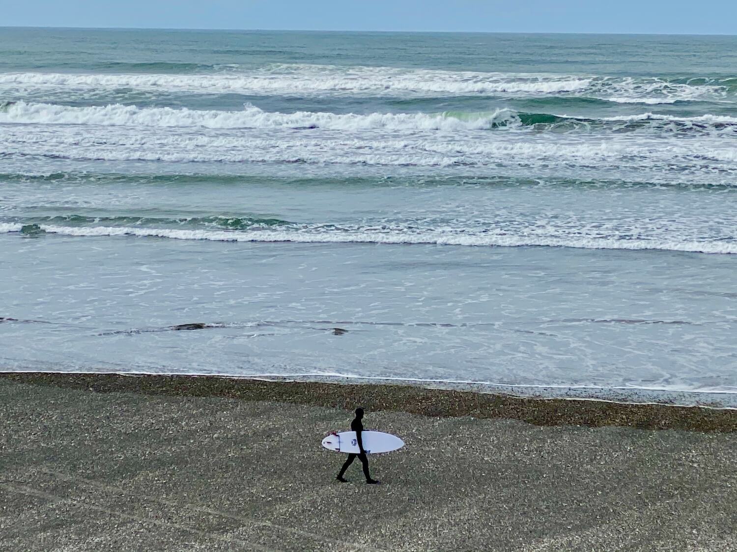 Westport Light State Park. A surfer wears a full body wet suit as he walks with a white surf board toward the waves of the Pacific Ocean near Westport, Washington.