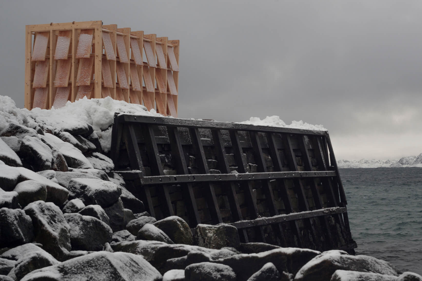 Sled House in position on a pier leading out to the North Atlantic Ocean in Greenland. A model of the Sled House, designed by architect Konstantin Ikonomidis for the Nuuk Nordisk 2019 festival in Greenland. The design is atop an actual sled created from wood and a structure with posts and slats only put together by rope and pegs fitting in holes.