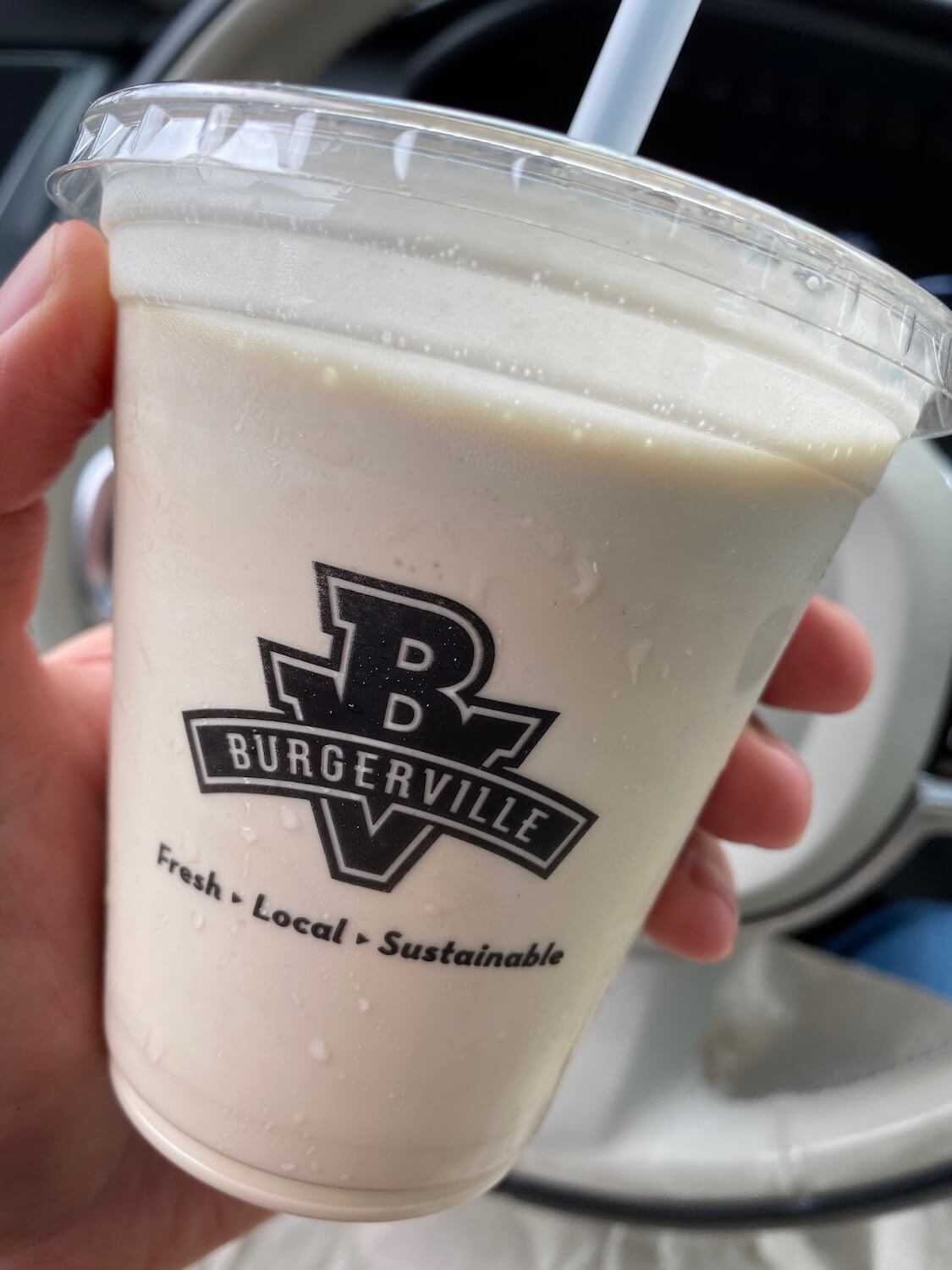 A burgerville milkshake is always welcome delight after a day trip.  Here, the plastic drink container shows the logo and name of Burgerville with a chocolaty substance that looks like a milkshake is inside.  