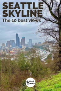 A sweeping view of the Seattle skyline from a panoramic viewpoint of Dr. Jose Rizal Park on Beacon Hill. The tall buildings of downtown Seattle rise in the background against gray stormy clouds and the grass is bright green on the hill with the trees in the foreground.