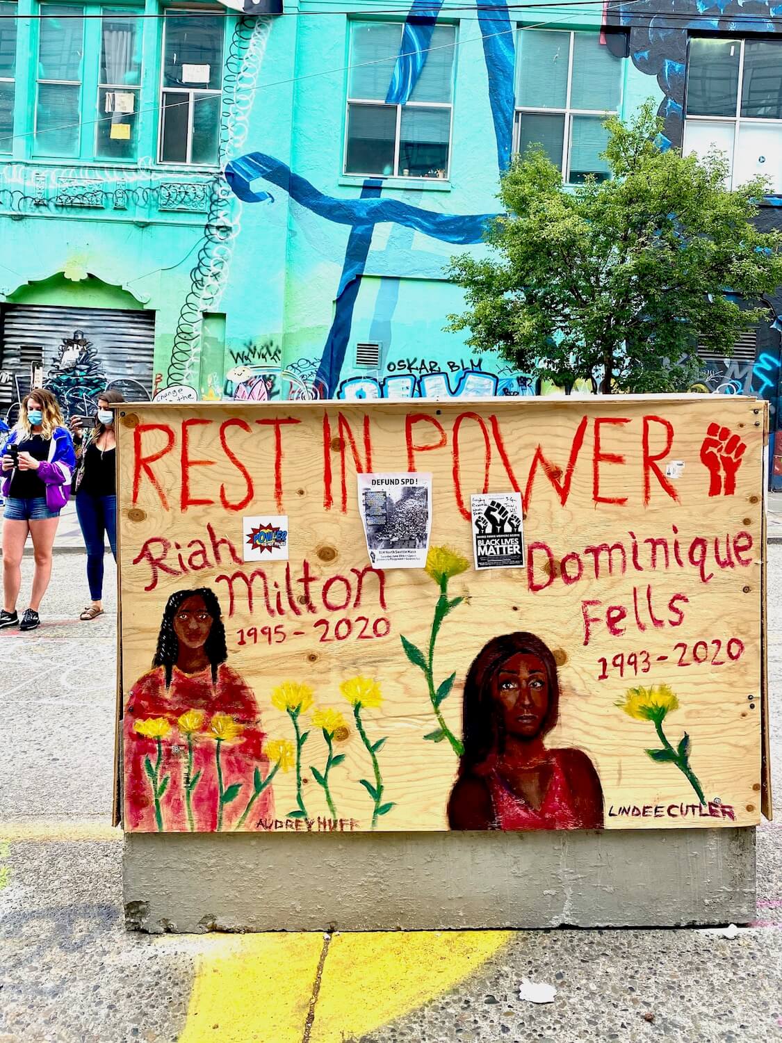 A row of concrete traffic barricades are covered in plywood and painted with a variety of messages. This is in the Black Lives Matter protest area of Capitol Hill in Seattle.  This sign says, Rest in Power and memorializes two black girls ages 15 and 17. 