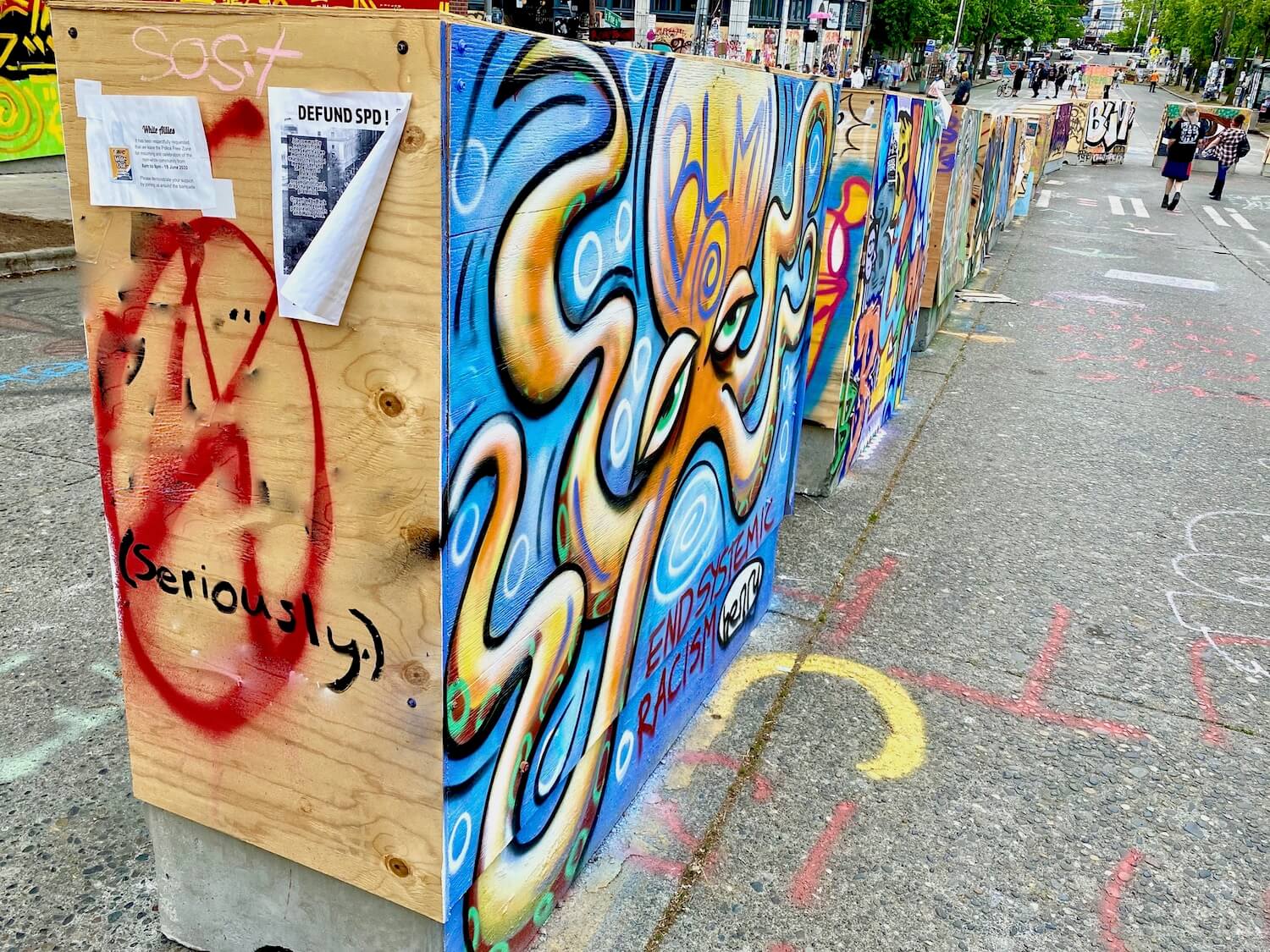 A row of concrete traffic barricades are covered in plywood and painted with a variety of messages. This is in the Black Lives Matter protest area of Capitol Hill in Seattle.
