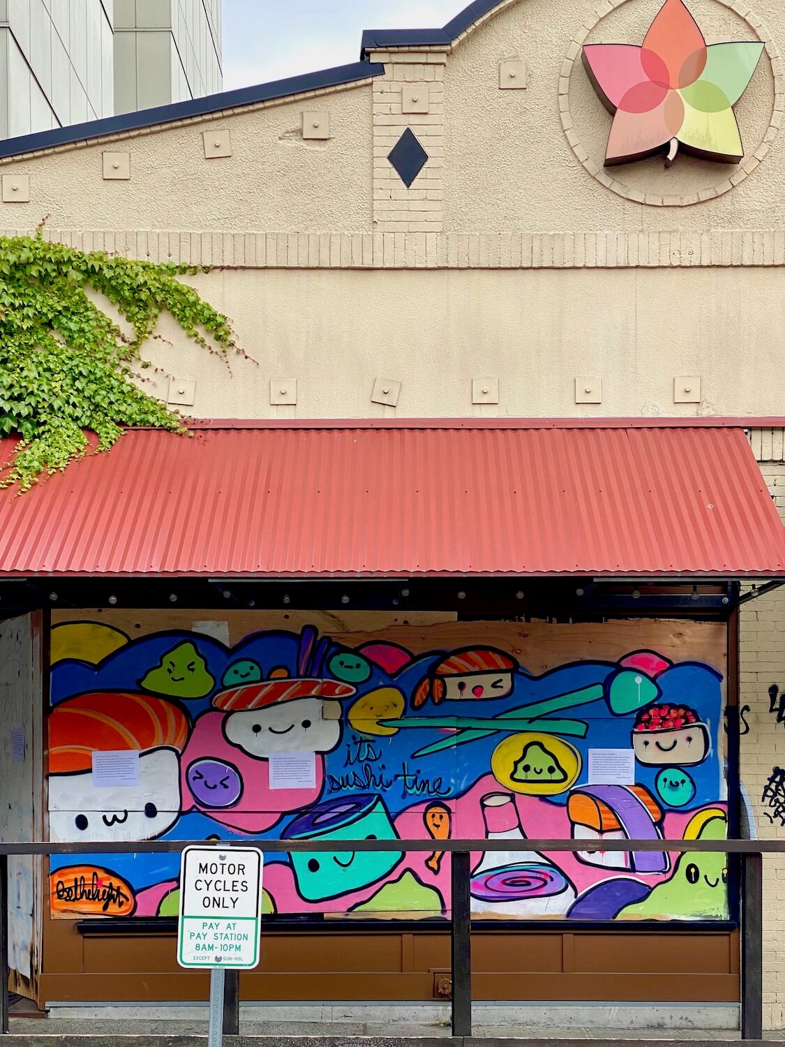 A former Japanese restaurant in the Capitol Hill area of Seattle is boarded up with a brightly covered mural with colorful pieces of sushi.