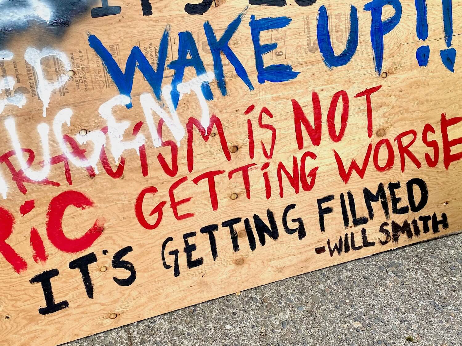 This plywood sign is in the CHOP area of Capitol Hill during the Black Lives Matter protest. The plywood is painted with blue letters that say, Wake up and red letters that say, Racism is not getting worse, it's getting filmed. By Will Smith.