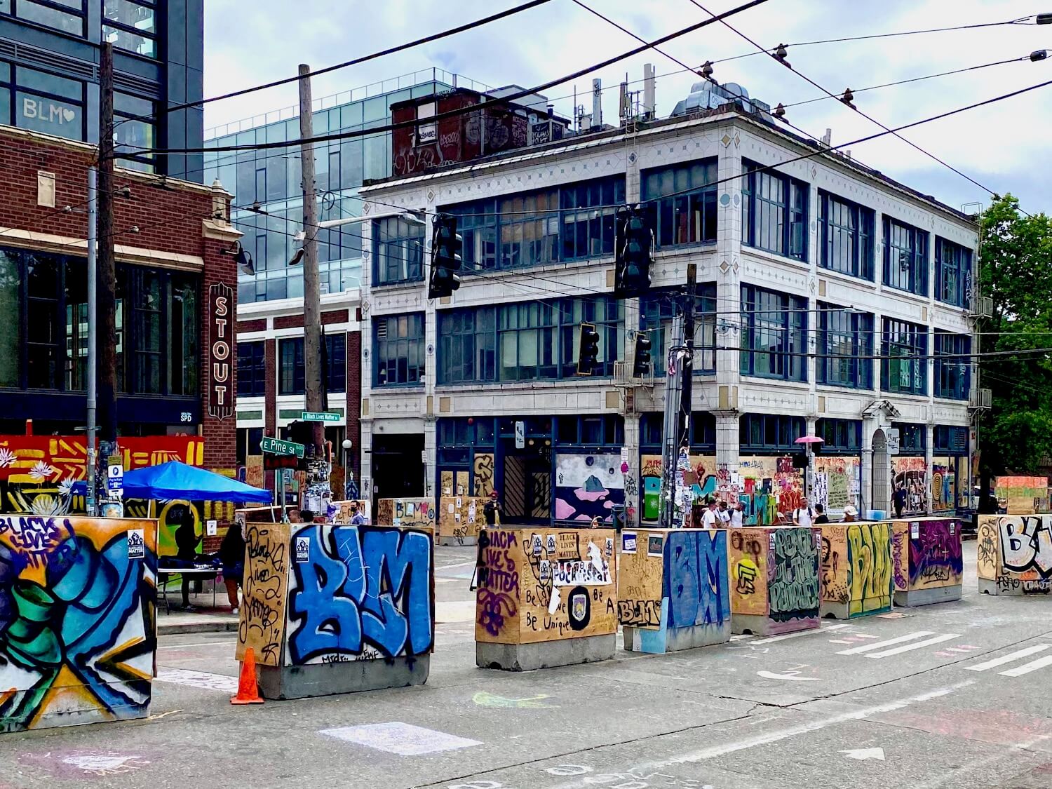 Signage at the CHOP area of Seattle during the Black Lives Matter protest. The concrete traffic barriers are covered with painted plywood depicting many different themes around the Black Lives Matters movement. In the background are multi-story buildings.