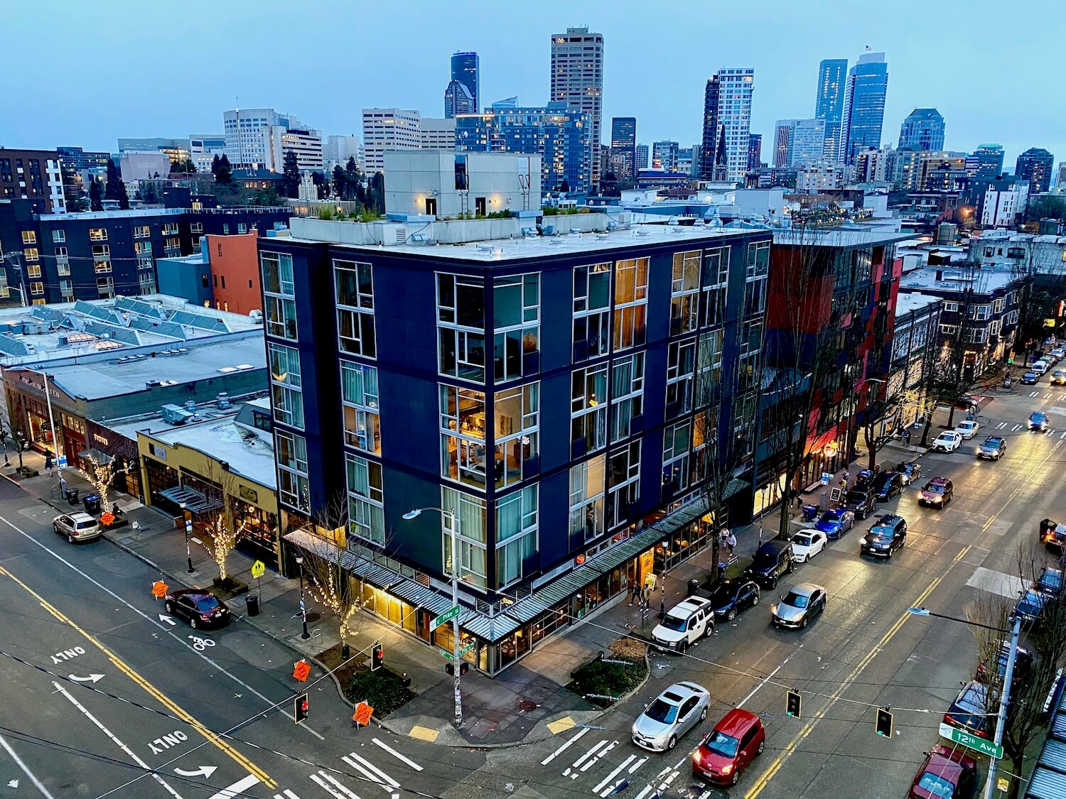 A view of buildings in the Capitol Hill neighborhood below. Cars are moving on the streets and the lights are just beginning to turn on for the evening.