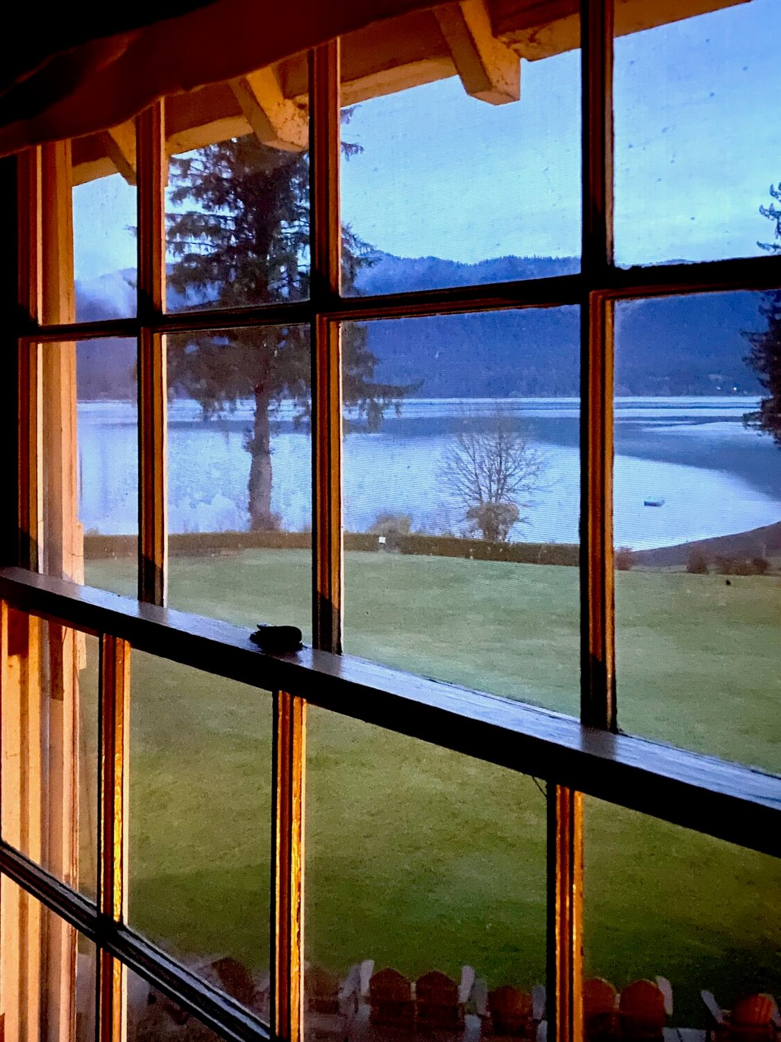 A sunrise view of Lake Quinault as viewed from one of the second story rooms in the historic lodge. The wood paned window reveals the green lawn flowing to the lake, just waking up for the day.