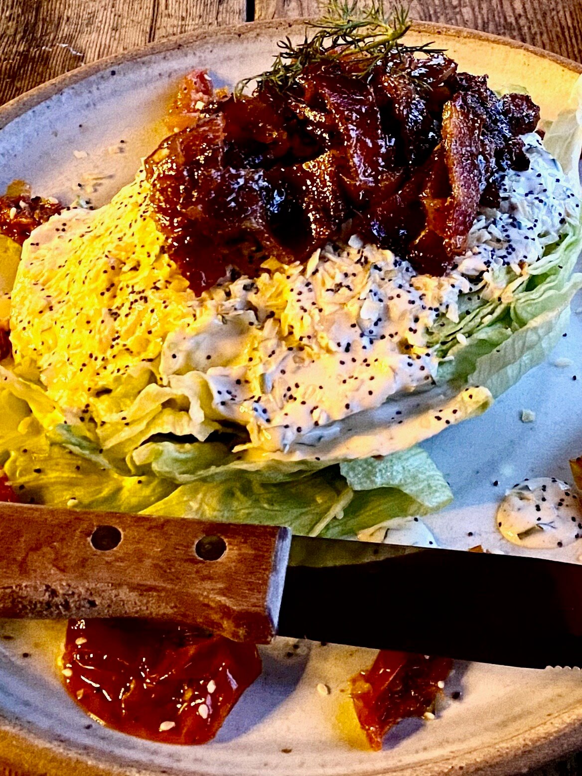 A close up of chop salad of iceberg lettuce with marinated bacon on top and a knife crosses the pottery plate covered some peeled dates.