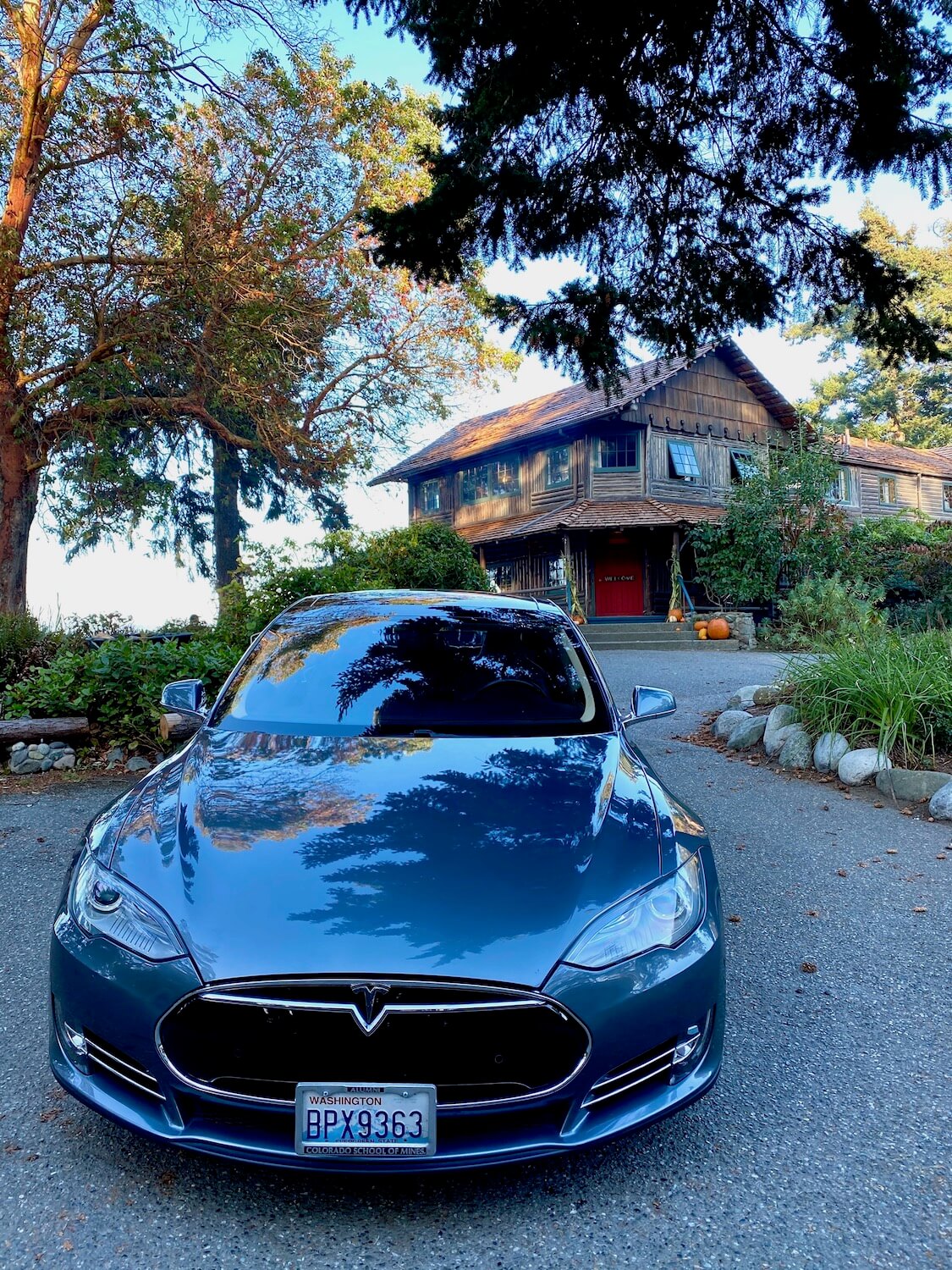 A Tesla electric vehicle is parked near the entrance to Captain Whidbey Inn on Whidbey Island in the middle of the Puget Sound.  The red door leading inside the hotel is bright against the log cabin style of the lodge.  