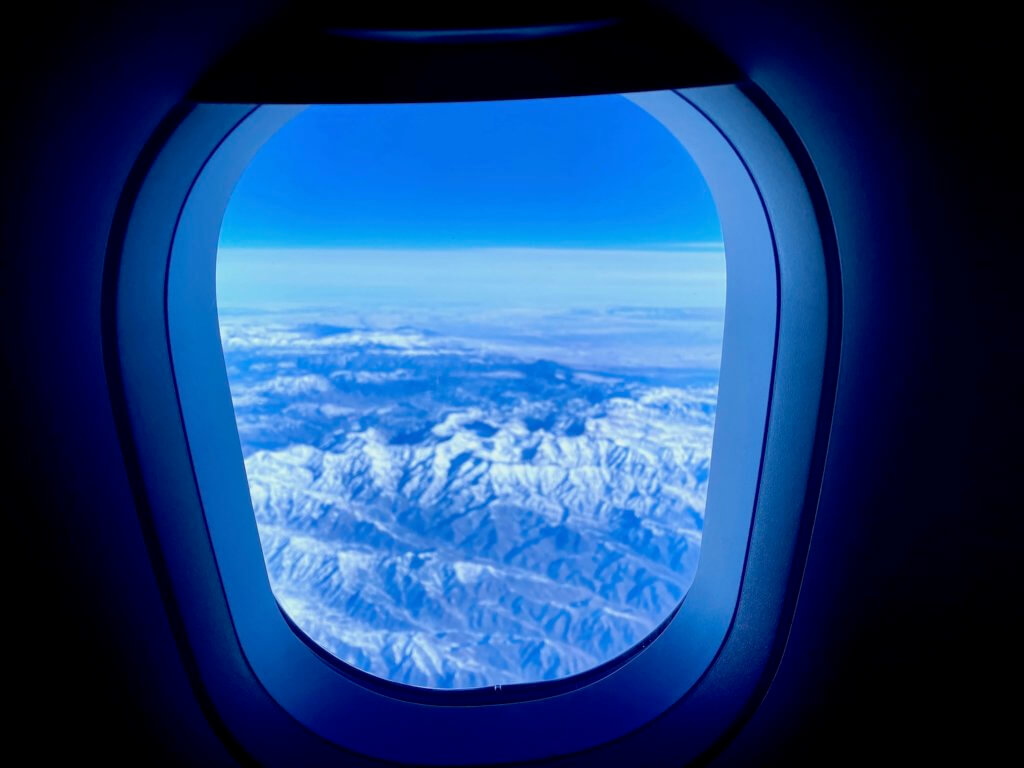 A view through an airplane window looking out at mountains covered in snow.