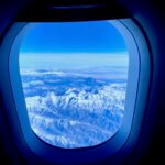 A view through an airplane window looking out at mountains covered in snow.