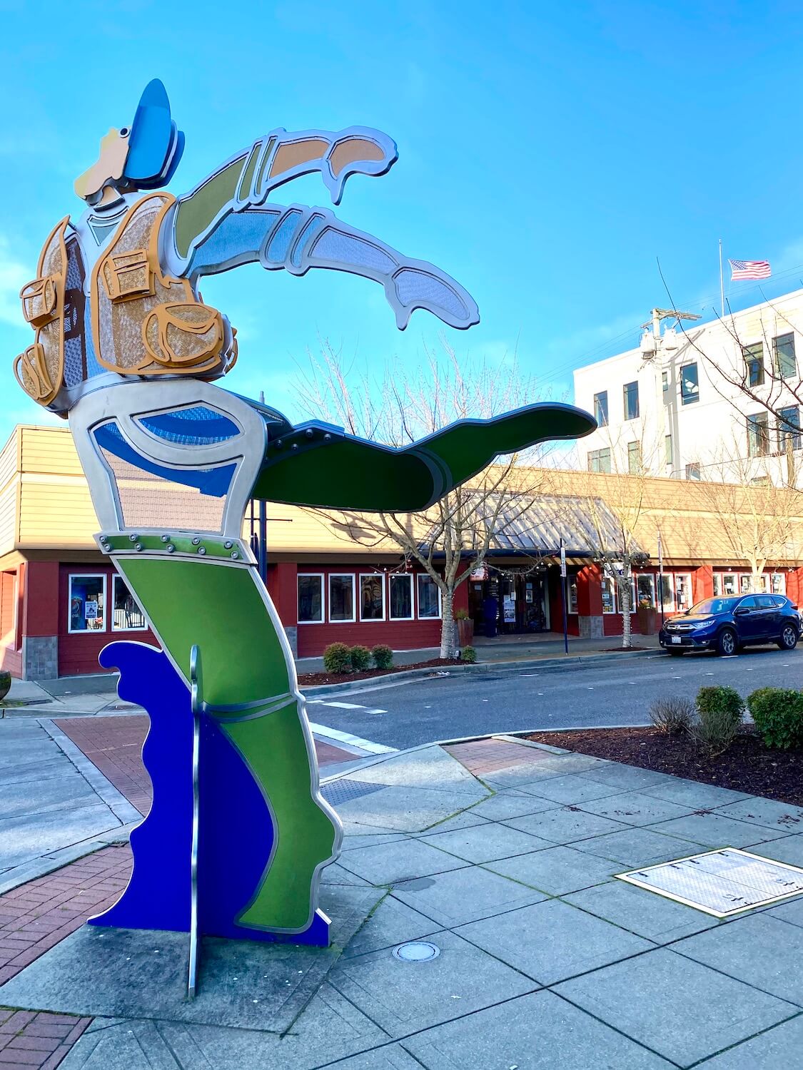 A brightly covered art installment along Pacific Avenue in downtown Bremerton.  An American flag waves in the background under a blue sky. 