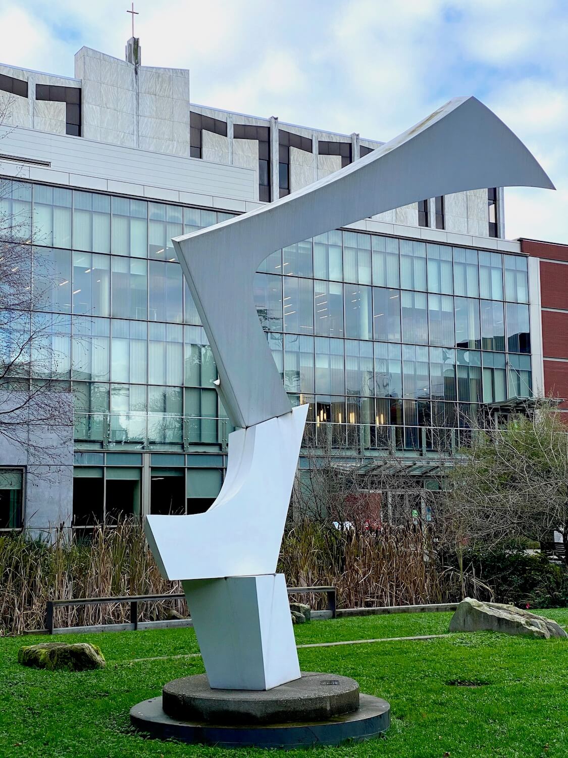 Art at Seattle University in the middle of the grass covered quad area. A large metallic sculpture is the centerpiece against shiny glass windows of the student union building.