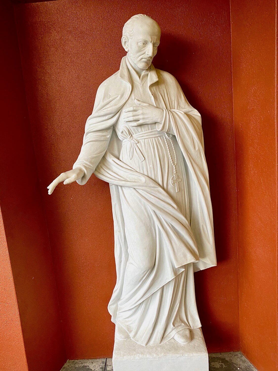 A white statue of St. Ignatius Loyola snuggles into an orange alcove of a building at Seattle University. 