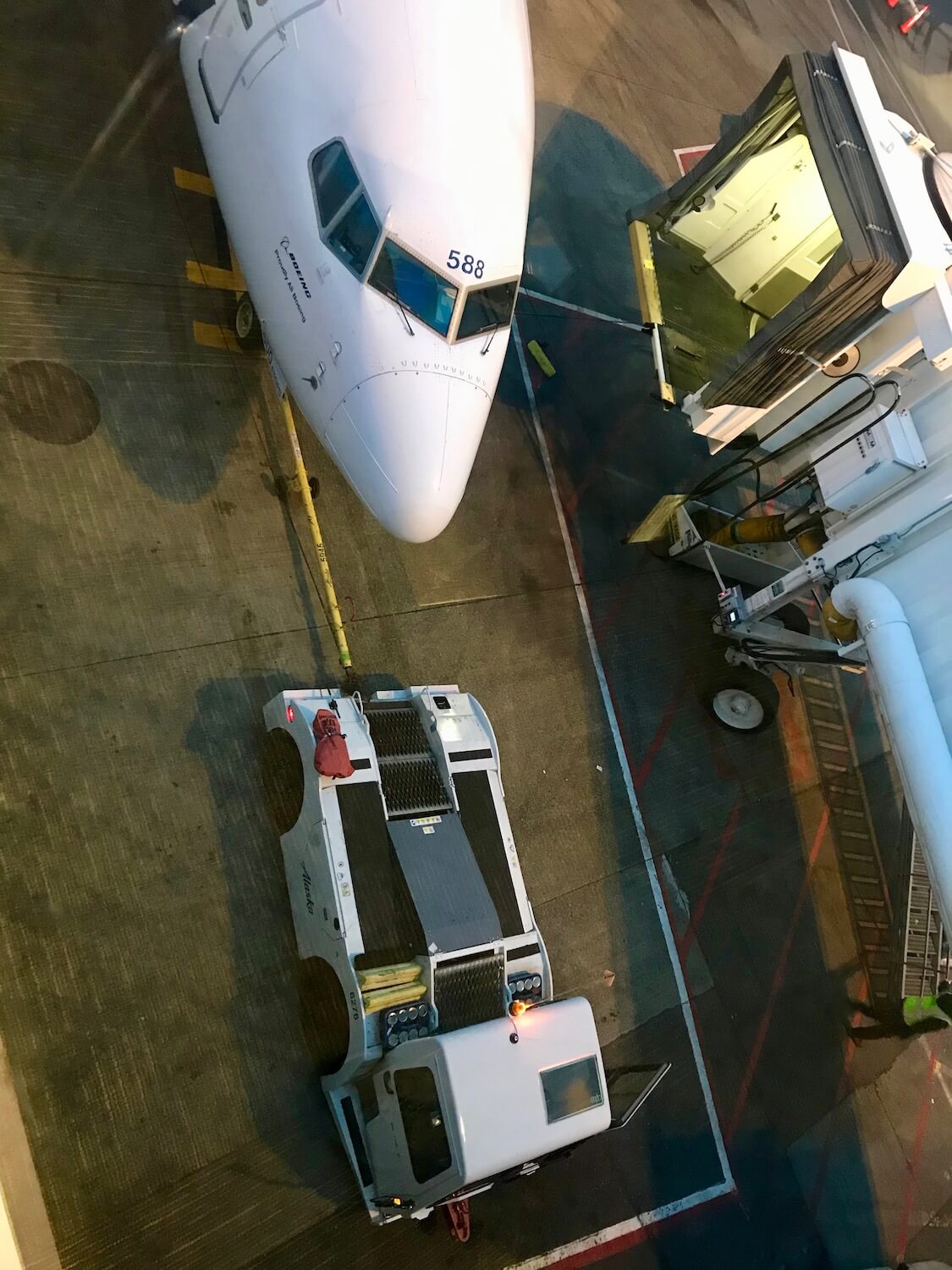 An airplane gets ready to push away from the gate by a tug.  The jetway has already been pulled away from the white nose of the plane.  