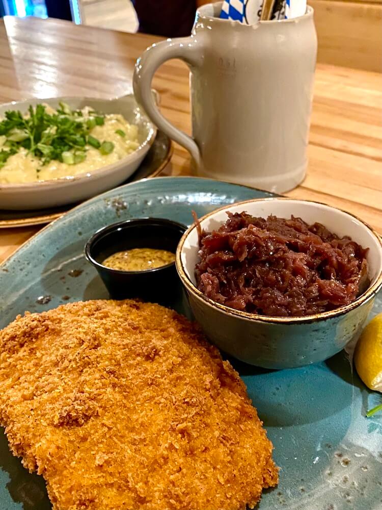 A German meal sits on a themed table next to a bier stein.  The schnitzel is breaded lightly and accompanied by yellow spicy mustard and cooked cabbage.  