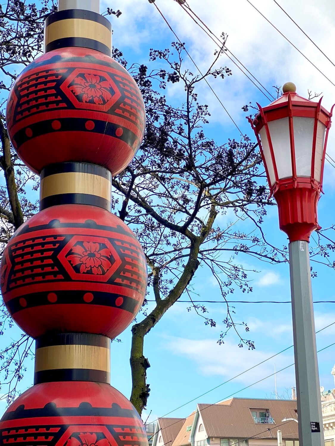 A Chinese lantern is next to a brightly painted red street lamp while a cherry blossoms begin to make their way out of a tree, waiting for Summer in Seattle. 