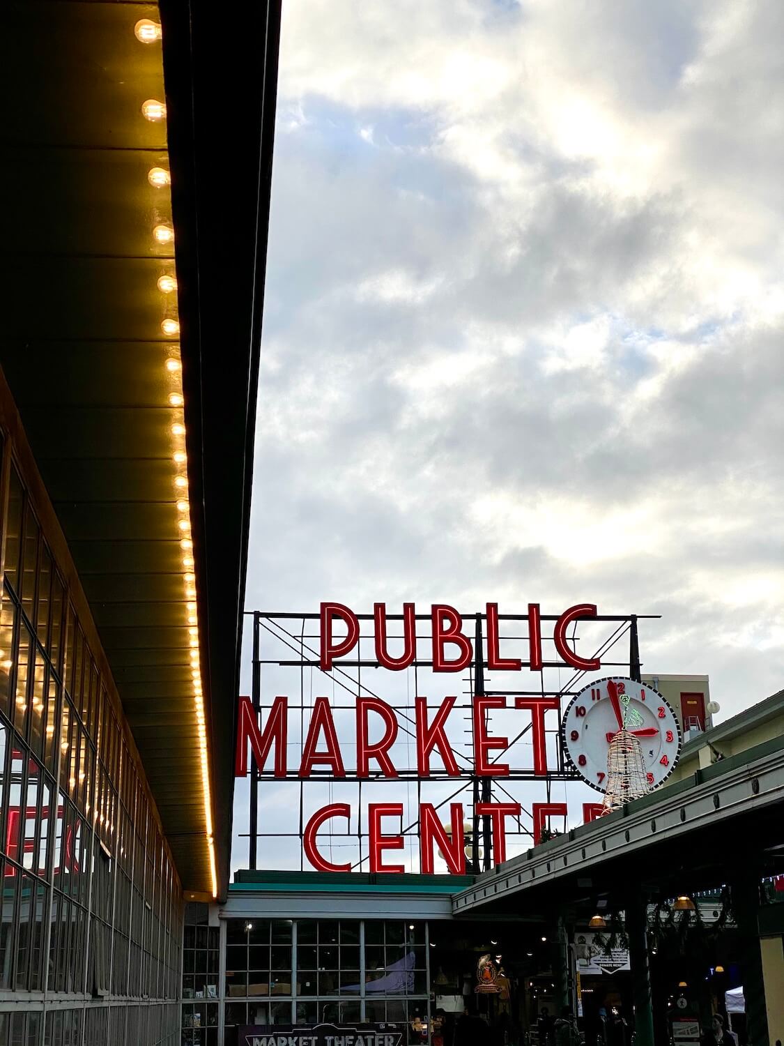 Pike Place Market sets up a moody scene with a string of light bulbs leading to the giant red neon sign that says, "Public Market Center."  The clouds are a swirl of gray above.