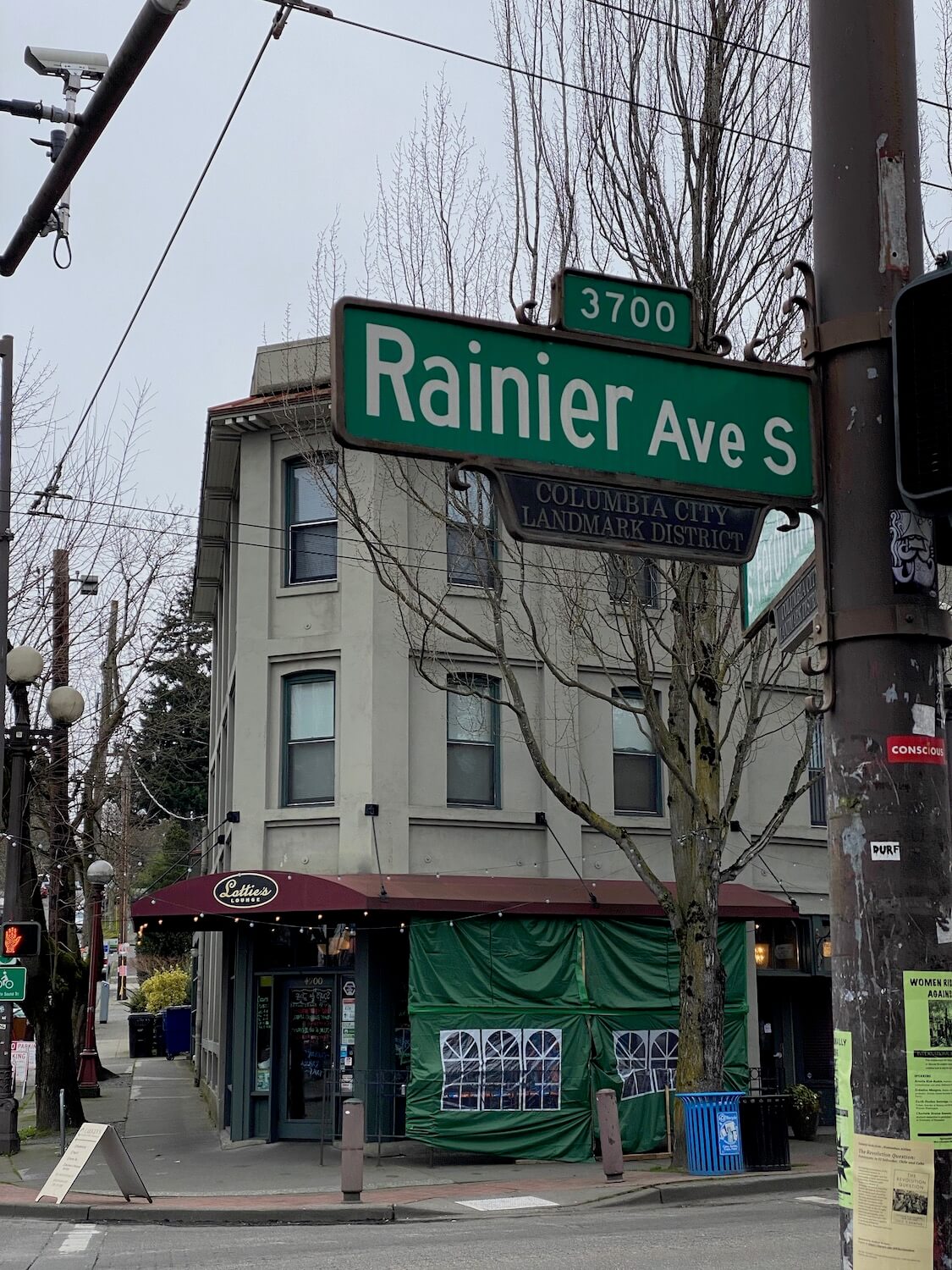 An up close photo of Rainier Ave S street sign in Columbia City district of Seattle.  In the background is a historic looking three story building and this area is a great place to spend time on a layover at Seatac Airport. 